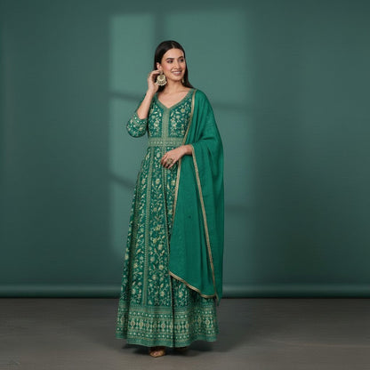Kurti Connection USA emerald green Anarkali suit with intricate gold embroidery and dupatta. Model wears statement earrings and ring.
